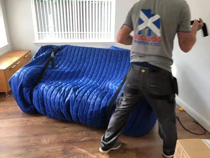 A team member moving a sofa wrapped in protective blankets